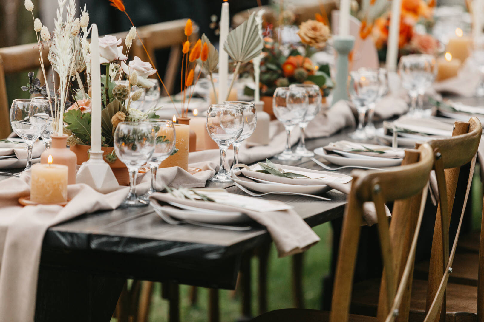 Event and catering agency organization modern wedding in boho style. Table for guests assembled with dishes, cutlery, glasses and flowers, candles and elements, chairs on green lawn, flat lay, outdoor